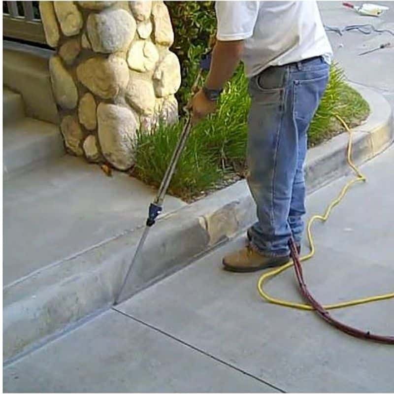 Worker pressure washing curb beside stone building