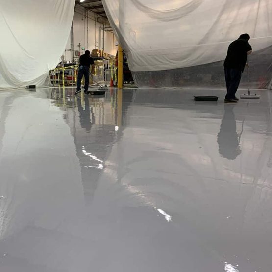 Workers applying epoxy coating on warehouse floor
